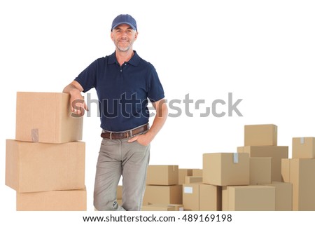 Happy delivery man leaning on pile of cardboard boxes against arrangements of cardboard boxes
