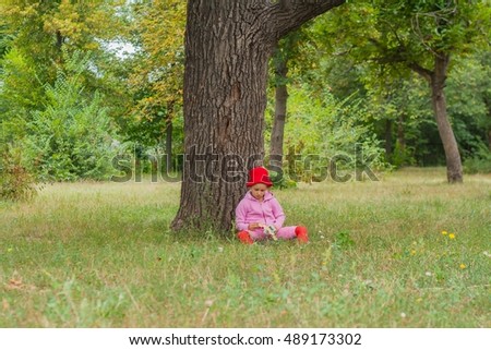 The child sits under a big oak. The girl plays plane model . The child in the park plays