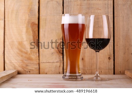 Tall glass of light beer and red wine glass over a textured wood background Royalty-Free Stock Photo #489196618