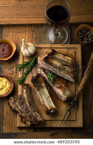 Pork ribs grilled with rosemary and a glass of wine on a wooden background