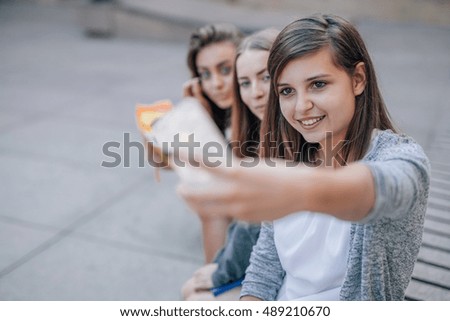 Young women are sitting at street stairs and taking selfie. City background