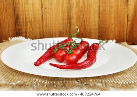 pods of chili peppers and branch of red cherry tomatoes on the plate