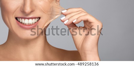 Portrait of brunette young Beautiful woman in facial peel off mask. Peeling. Beauty girl and body skin care. Isolated on grey background. Studio shot. Pull piece of leather to the side. Hand holding Royalty-Free Stock Photo #489258136