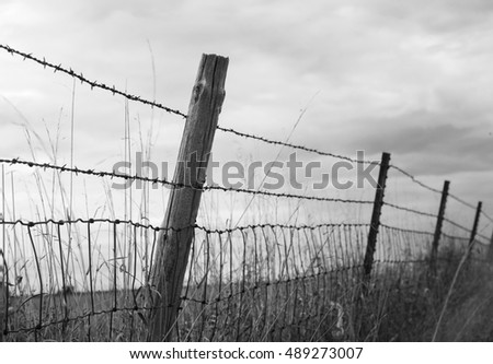 A black and white photograph of a barb wire fence leading down the horizon of an open field.