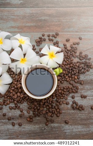 Green cup of coffee with plumeria flower and coffee bean on wood vintage background, hipster lifestyle, flat lay image and copy space