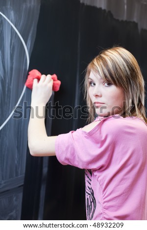 pretty young college student erasing the chalkboard/blackboard in a classroom, looking at you