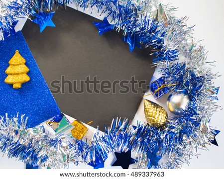 Christmas or New Year flat lay composition. Blue sparkling ribbon wreath. Gold fir tree toy, ornament, blue gift. Black paper with blank page. Season background for winter holidays or marketing event