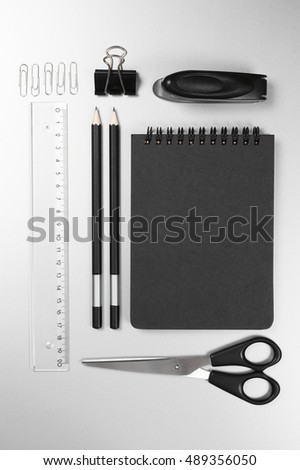 Black stationery on gray desk: notepad, pencils, scissors, stapler, clip, pins, ruler. Top view point.