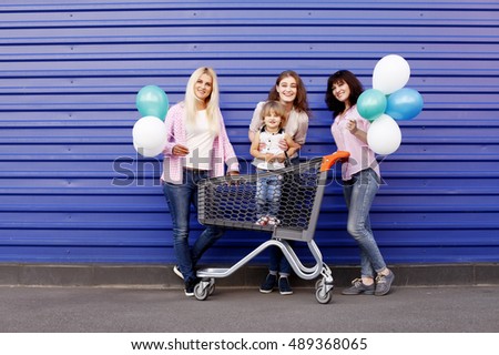 Conceptual photo of happy loving family. Mother and her two daughters children girls and granddaughter with shopping cart and balloons. Outdoors