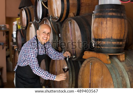 Cheerful male wine maker taking wine from wood in winery Royalty-Free Stock Photo #489403567