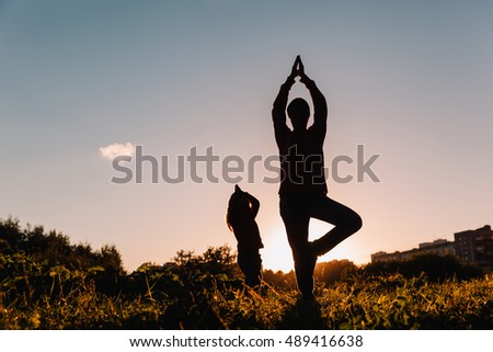 father and little daughter doing yoga at sunset