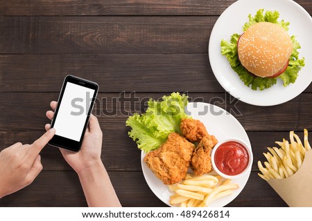 Using smart phone with burger, french fries and fried chicken set on wooden background.