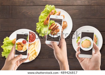 Friends using smart phones to take photos of sausage, pork chop, Fries chicken and burger.
