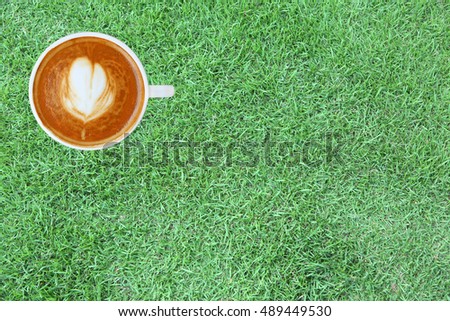 Top view of a coffee with heart pattern in a white cup on green grass background, latte art