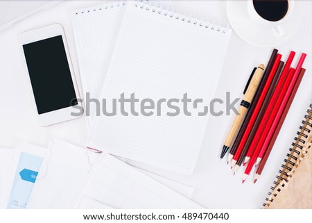 Top view and close up of white office desktop with blank notepad, other supplies, smartphone and coffee cup. Mock up