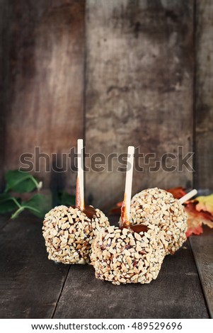 Three candy apples with nuts and caramel against a rustic wooden background. Shallow depth of field with selective focus on foreground.