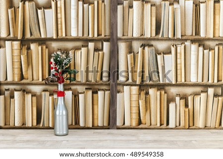 Christmas decoration of a silver bottle, fir cone and red berries, placed by a bookshelf