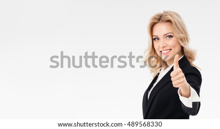Happy smiling beautiful young businesswoman showing thumbs up gesture, on grey background with blank copyspace area for slogan or text message. Caucasian blond model in business presentation concept. 