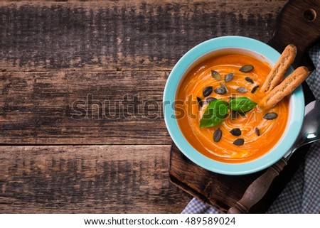 Roasted pumpkin and carrot soup with cream and pumpkin seeds on rustic wooden background.