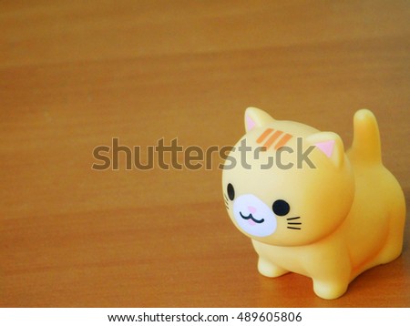 Funny miniature cat made from plastic on brown / wood ground. Closeup view with cat on the right.
