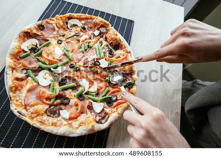 woman hands Slicing fresh pizza with beans, cheese, ham, eggs, pepperoni and vegetables. Cutting pizza