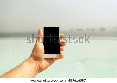 technology, travel, tourism, communication and people concept - close up of male hand holding smartphone with blank screen on summer beach