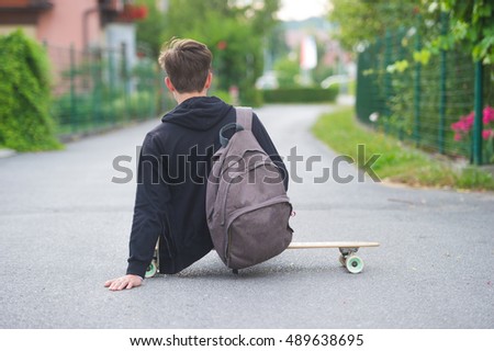 Teenager sitting on his longboard on the street. 