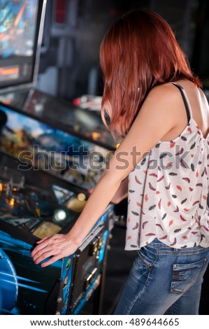 Young woman playing on the pinball machine in game room Royalty-Free Stock Photo #489644665
