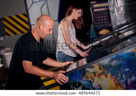People playing pinball at arcade in game room Royalty-Free Stock Photo #489644671