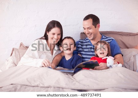 Parents and two young children looking at picture book in bed