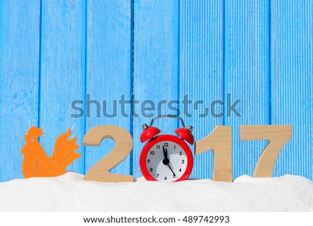 Rooster, symbol of 2017 on the Chinese calendar. Rooster and the numbers 2017 in a snowdrift on a blue wooden background