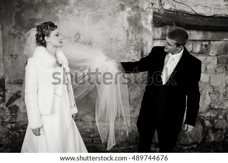 Groom holds bride's veil while they stand in old stone alley