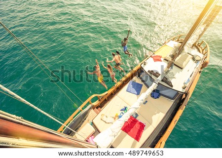Aerial view of young people jumping from sailing boat on sea trip - Rich happy friends having fun in summer party day - Exclusive vacation concept - Warm vintage filter with enhanced sun flare halos Royalty-Free Stock Photo #489749653