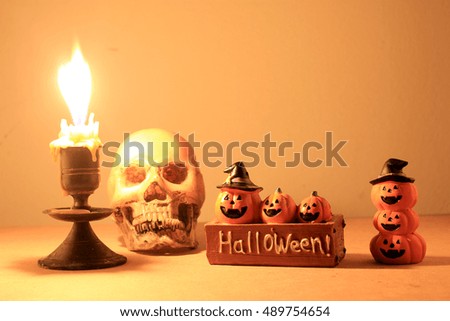 Still Life of skull, candle and Pumpkin with light candle tone on wooden table over orange background in night time.