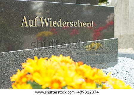 Grave in the German cemetery. See you again! text in German on a gray granite gravestone with flower reflection. All saints day
