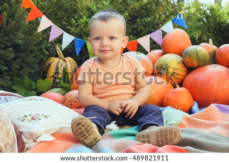 Little cute boy playing on the plaid near the orange pumpkins.  Smiling baby boy among the pumpkins on Halloween day.