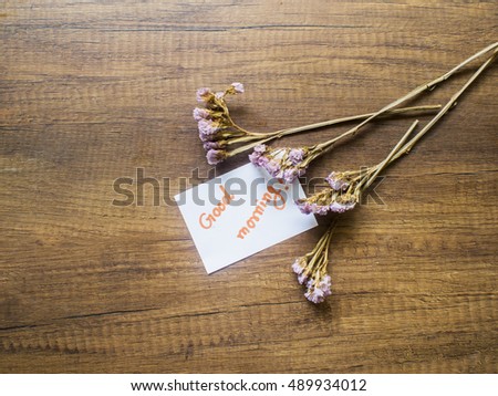 Flower and piece of paper with text "good morning" on the wooden table close-up