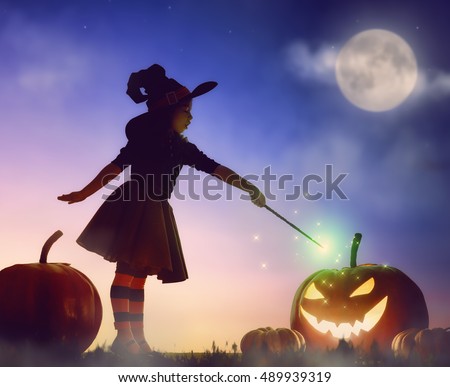 Happy Halloween! Cute little witch with a big pumpkin. Beautiful young child girl in witch costume outdoors. 