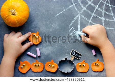 Happy halloween! Child draws with chalk spider web on the table with pumpkins. Kids preparing for Halloween