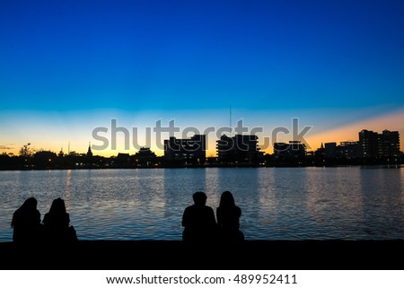 Young couple watching a sunset behind a cityscape sitting on a quay of a river. Subtle vintage filter applied. Young couple sitting near the city and watching the sun.