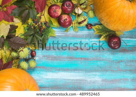 Frame made of autumn leaves, pumpkins, apples, chestnuts and wild grapes on old wooden background. Copy space.
