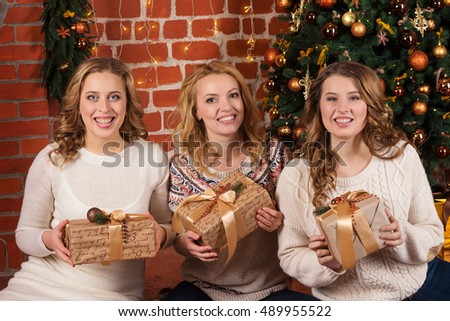 three pretty women open gifts near christmas tree