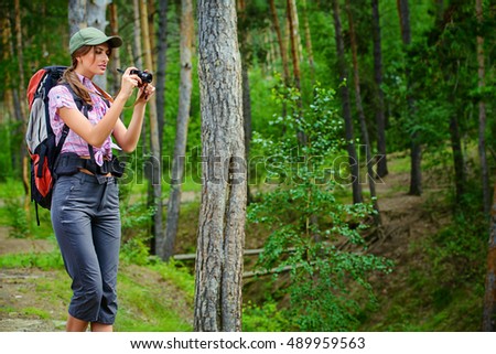 Adventure concept. Happy young woman hiking in the forest. She takes pictures of nature. Active lifestyle, tourism. Tourist equipment.