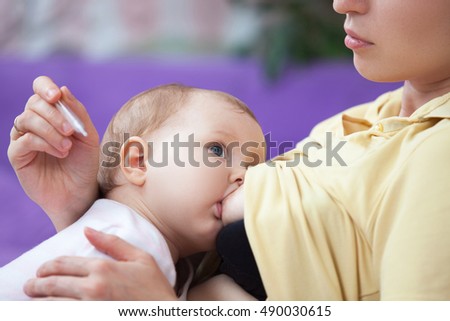 A young woman breast-feeding a baby, and measure its temperature