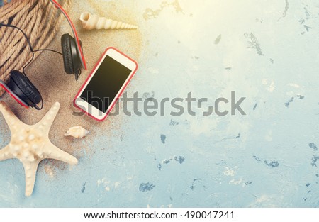 Travel vacation items on stone background. Smartphone, headphones and starfish. Top view with copy space. Sunny toned