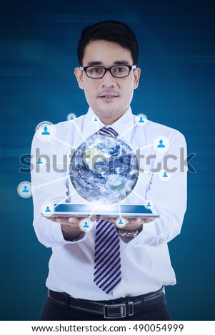 Young businessman presenting 3d earth globe in tablet, shot with blue background