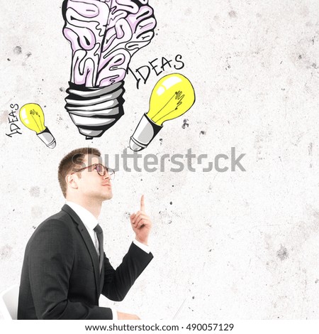 Handsome businessman in glasses pointing at creative light bulb brain sketch. Ideas and brainstorming concept