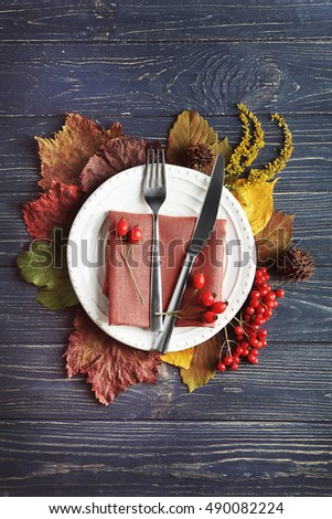 Autumn composition of leaves, berries, plate, knife and fork on wooden background. Thanksgiving day concept