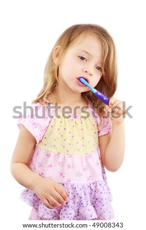 Cute little girl in pink pajamas is brushing her teeth against a white background.