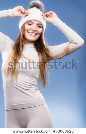 Attractive woman in winter cap and gray sports thermolinen underwear for skiing training studio shot on blue. Long sleeves top and leggings
